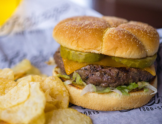 hamburger with cheese, lettuce, pickles, and chips